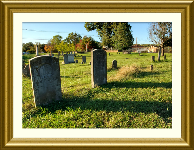 The sun backlights two headstones at Old Harmony Cemetery, casting a long shadow on the grass.